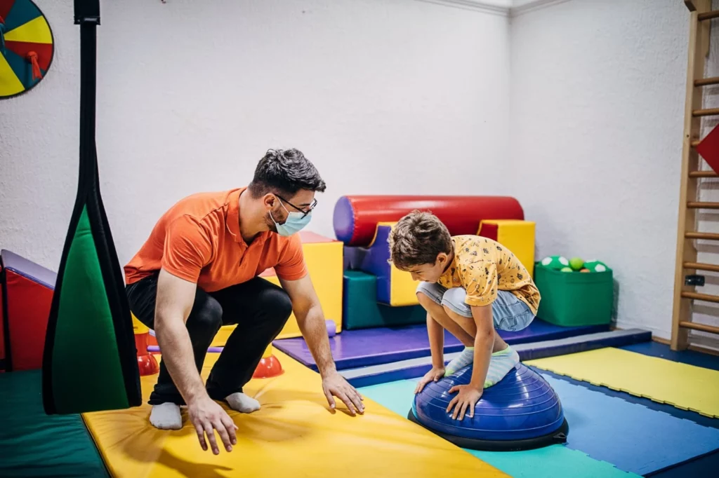 Image of a therapist providing support and guidance to a small boy during a physical therapy exercise