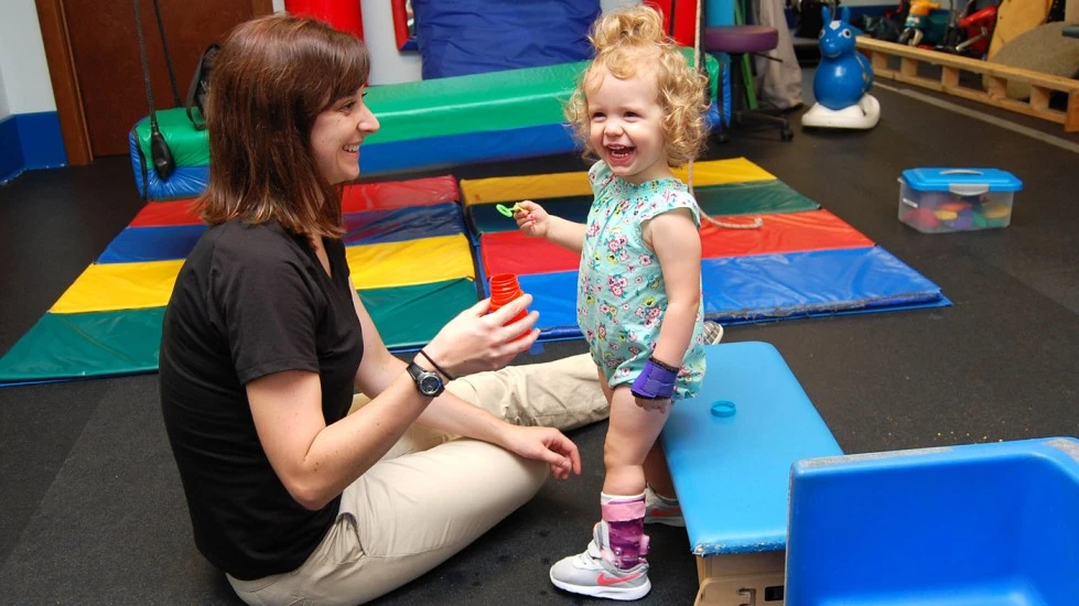 Image of a little girl engaging in physical therapy with her therapist, sharing laughter and joy