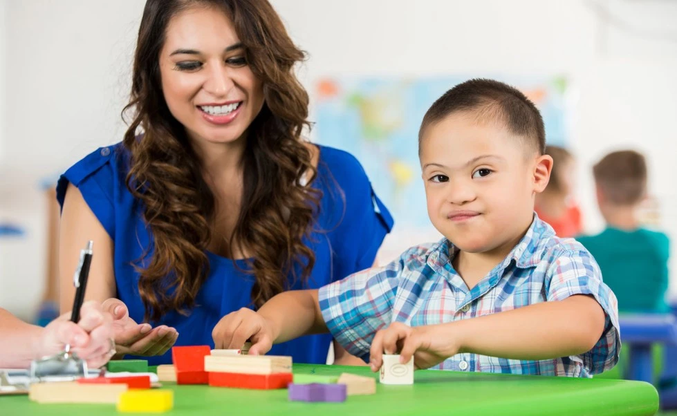 Image of a teacher providing support and guidance to a child with special needs in an inclusive classroom