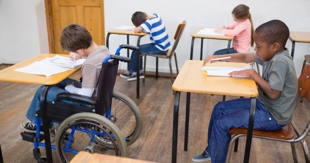Image of a child in a wheelchair sitting comfortably at a desk in a well-equipped classroom