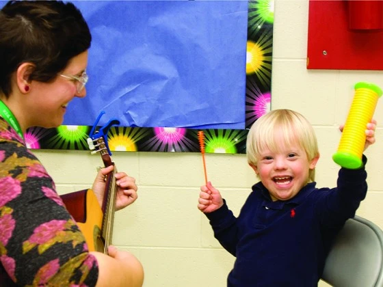A boy with special needs participating in music therapy with teacher strumming a guitar