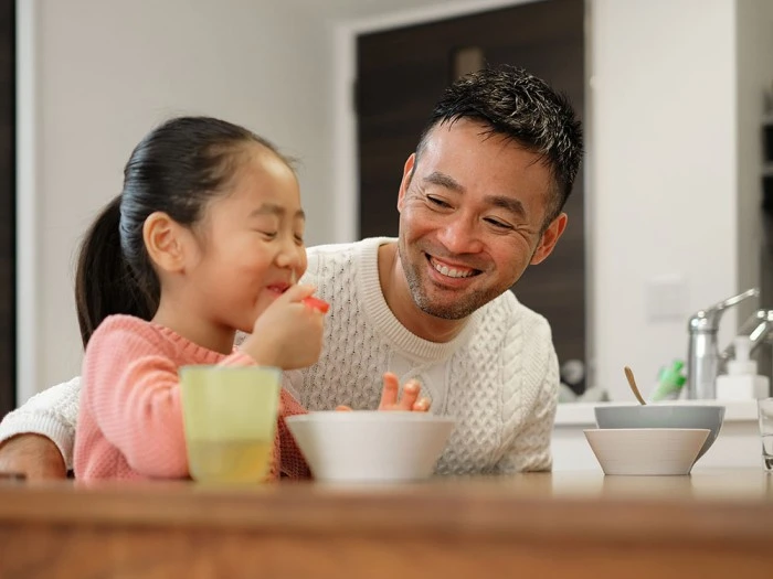 A child happily eating a meal with her father, emphasizing the role of nutrition in family relationships.